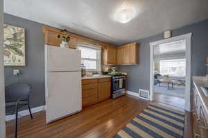 Kitchen with freestanding refrigerator, stainless steel gas range, dark wood-style floors, light countertops, and plenty of natural light