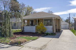 View of front facade with an outdoor structure, brick siding, a porch, and a detached garage