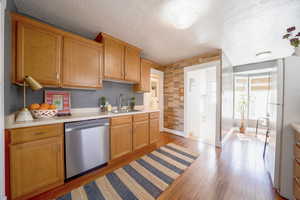 Kitchen with light countertops, freestanding refrigerator, dishwasher, light wood-type flooring, and a textured ceiling