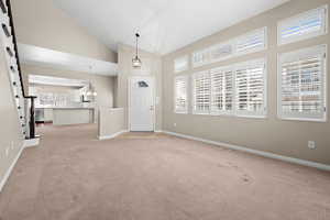 Foyer entrance featuring vaulted ceiling, light colored carpet, and hanging lights