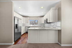 Kitchen featuring a peninsula, stainless steel appliances, white cabinetry, backsplash, and light stone counters