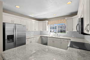 Kitchen featuring stainless steel appliances, white cabinetry, light stone countertops, backsplash, and recessed lighting