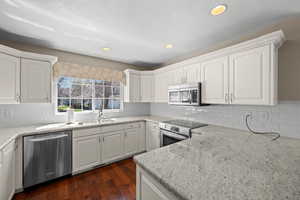 Kitchen with white cabinetry, stainless steel appliances, light stone counters, dark wood-type flooring, and recessed lighting