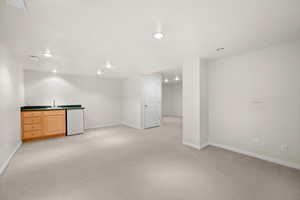 Indoor wet bar featuring dark countertops, light wood finish cabinetry, light carpet, recessed lighting, and white refrigerator