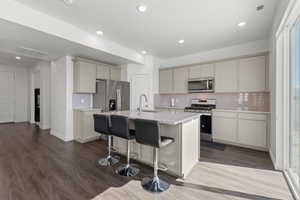 Spacious kitchen featuring LVP flooring, light gray cabinetry, granite countertops, stainless steel appliances, large island and tile backsplash