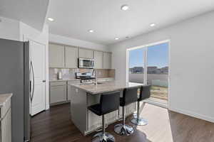 Spacious kitchen with sliding door to back patio, featuring LVP flooring, light gray cabinetry, granite countertops, stainless steel appliances, large island and tile backsplash