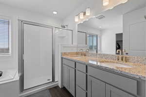 Primary ensuite bathroom featuring LVP flooring, gray cabinetry, granite countertops with dual sinks, and a separate tub and shower