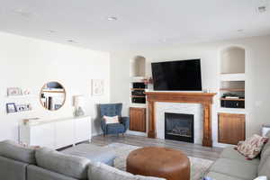Living area featuring built in features, wood finished floors, a glass covered fireplace, and recessed lighting