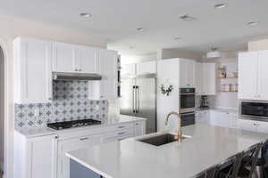 Kitchen featuring open shelves, white cabinets, built in appliances, and a center island with sink