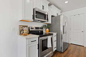 Kitchen featuring stainless steel appliances, white cabinets, dark wood finished floors, recessed lighting, and light stone counters