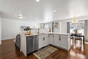 Kitchen featuring a kitchen island with sink, stainless steel dishwasher, white cabinets, dark wood-style flooring, and a textured ceiling