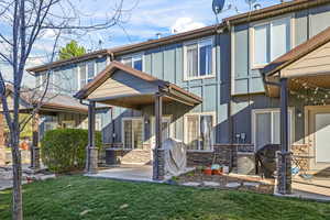 Rear view of house featuring stone siding, a yard, and a patio