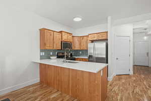 Kitchen with a peninsula, light wood-style floors, stainless steel appliances, backsplash, and light stone countertops