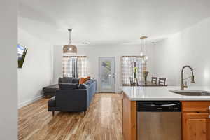 Kitchen featuring dishwasher, light wood finished floors, open floor plan, hanging light fixtures, and light stone countertops