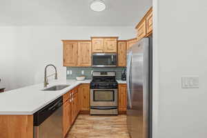 Kitchen featuring stainless steel appliances, light wood-type flooring, a peninsula, tasteful backsplash, and light stone countertops