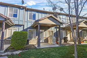 View of front of home with stone siding, a patio area, and a front lawn