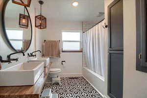 Full bathroom with double vanity, shower / bathtub combination with curtain, and light tile patterned flooring