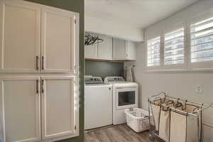 Laundry room with cabinet space, light wood-style floors, and washing machine and clothes dryer