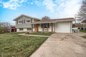 Tri-level home with brick siding, covered porch, a garage, driveway, and a front yard
