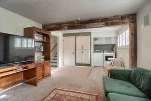 Living area featuring light colored carpet, washing machine and dryer, and a textured ceiling