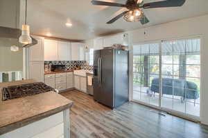 Kitchen with stainless steel appliances, white cabinets, backsplash, light wood-type flooring, and recessed lighting