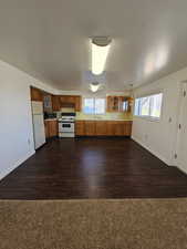 Kitchen featuring glass fronted cabinets, white appliances, wood finish cabinetry, light countertops, and decorative light fixtures