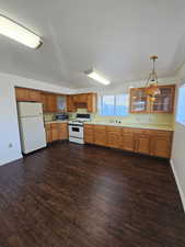 Kitchen featuring light countertops, hanging light fixtures, white appliances, and wood finish cabinets