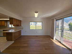 Dining area featuring wood finish cabinetry, a peninsula, light countertops, stainless steel dishwasher, and light wood-type vinyl laminate flooring