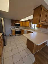 Kitchen featuring light countertops, stainless steel appliances, a peninsula, and wood finish cabinets