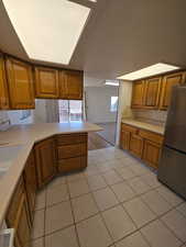 Kitchen featuring wood finish cabinets, light countertops, freestanding refrigerator, and a peninsula