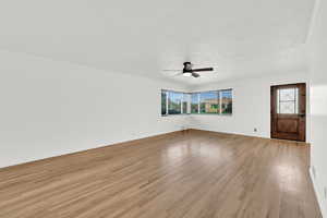 Unfurnished living room with light wood-style floors, a textured ceiling, and ceiling fan