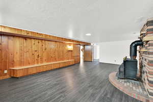 Finished below grade area with dark wood-style floors, a wood stove, a textured ceiling, and wood walls