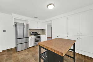Kitchen featuring stainless steel appliances, white cabinetry, light countertops, stone finish flooring, and backsplash