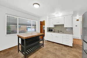 Kitchen with light countertops, white cabinets, decorative backsplash, freestanding refrigerator, and white microwave