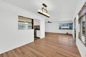 Unfurnished living room featuring crown molding, light wood finished floors, healthy amount of natural light, and ceiling fan