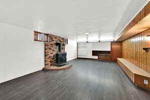 Finished basement featuring wooden walls, dark wood-style floors, a wood stove, and a textured ceiling
