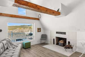 Living area with a tiled fireplace, vaulted ceiling with beams, and wood finished floors