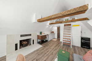 Living room with a tiled fireplace, light wood-style flooring, and lofted ceiling