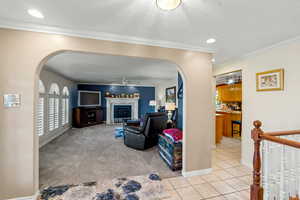 Living room with arched walkways, crown molding, a textured ceiling, light tile patterned floors, and ceiling fan