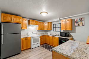 Downstairs Kitchen with black appliances, a textured ceiling, light wood finished floors, and wood finish cabinets