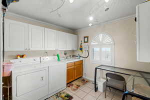 Main floor laundry area with light tile patterned floors, cabinet space, washer and dryer, and crown molding