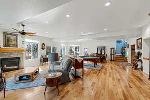 Living area featuring a stone fireplace, a textured ceiling, light wood-style floors, billiards table, and ceiling fan