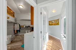 Walk in closet with light wood finished floors, washer / clothes dryer, and lofted ceiling