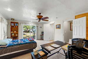 Main floor Owner's suite featuring a ceiling fan, access to exterior, light carpet, ornamental molding, and a textured ceiling