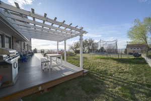 Fenced backyard with a trampoline, a storage unit, a pergola, a wooden deck, and outdoor dining area