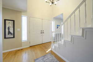 Entrance foyer with light wood finished floors, ornamental molding, hanging lights, a high ceiling, and healthy amount of natural light