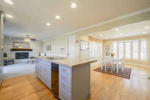 Kitchen with open floor plan, a fireplace with raised hearth, a kitchen island, light wood-style flooring, and ornamental molding