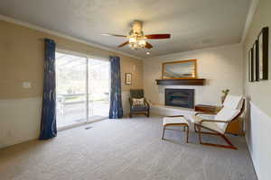 Sitting room featuring a textured ceiling, crown molding, a glass covered fireplace, a ceiling fan, and carpet