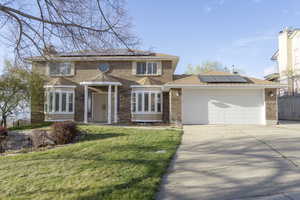 View of front of house featuring solar panels, brick siding, a front yard, and concrete driveway
