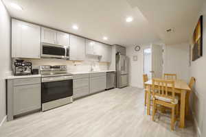 Kitchen with stainless steel appliances, light countertops, light wood finished floors, gray cabinetry, and recessed lighting